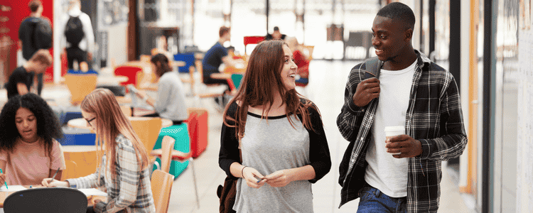 Two students smile and chat while walking through a cafeteria